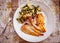 Grilled fish fillet and scrambled eggs and vegetables on plate, top view