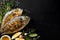 Grilled fish, sea bream with additions, herbs, olive oil, spices on a black background. Composition in the bottom left corner