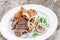 Grilled meat on plate, chicken legs, beef steak and onion on wooden background close up.