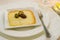 Grilled melted gruyere cheese appetiser topped with black and greeen olives on a square plate