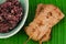 Grilled pork with bamboo stick and black sticky rice on banana leaf.