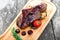 Grilled Ribeye Steak on bone with berry sauce, potatoes, tomatoes and rosemary on cutting board on wooden background close up