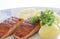 Grilled salmon fish filets on a plate with potatoes, parsley and slices of lemon. Close up stock photo with white back