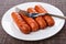 Grilled sausages, fork in plate on dark mat