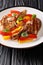 Grilled spicy pork chop with stewed yellow and red bell peppers and onions close-up in a plate. vertical