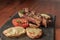 Grilled steak with legs and tomato on stone plate with wooden table. American food concept