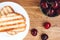 Grilled toast sandwich with egg on a white plate and red cherries in a cup on a wooden background