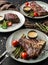 Grilled tomahawk meat medium rare, rib eye steak, beefsteak on plates with tomatoes, asparagus and berry sauce on dark wooden