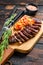 Grilled top sirloin cap or picanha steak on a cutting board with herbs. Dark wooden background. Top view