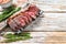 Grilled top sirloin cap or picanha steak on a meat cleaver with herbs. White wooden background. Top view. Copy space