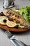 Grilled trout in brown clay bowl close-up. Front view of plate with grilled trout garnishe with salade, lemon and olives. Focus on