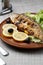 Grilled trout in brown clay bowl close-up. Front view of plate with grilled trout garnishe with salade, lemon and olives. Focus on