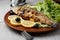 Grilled trout in brown clay bowl close-up. Front view of plate with grilled trout garnishe with salade, lemon and olives. Focus on