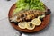 Grilled trout in brown clay bowl close-up. Front view of plate with grilled trout garnishe with salade, lemon and olives. Focus on