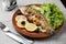 Grilled trout in brown clay bowl close-up. Front view of plate with grilled trout garnishe with salade, lemon and olives. Focus on