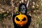Grim reaper holding halloween pumpkin head. Man in death mask with fire flame in eyes on nature autumn yellow dry leaves