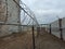 Grim view of barbed wire and gray fence. Abandoned building. Ominous sky, cloudy day