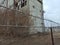 Grim view of barbed wire and gray fence. Abandoned building. Ominous sky, cloudy day