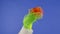 The Grinch's green haired hand holds out a white gift box with a orange bow on an isolated blue background. Gift