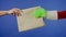 The Grinch's green haired hand reaches out and a man's hand takes a paper bag on an isolated blue background