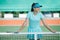 Grinning teenage girl standing on tennis court, leaning on the net, resting