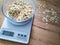 Grits weighing in glass bowl on the kitchen scales on wooden table.