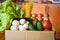 Groceries in paper box, basket with fresh vegetables and fruits on yellow background