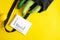 Grocery list in paper notepad and cotton eco black bag with zucchini and cucumber, lemon on yellow background with copy space