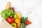 Grocery paper bag full of fresh fruits and vegetables on white marble background. Shopping and delivery service concept.