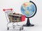 Grocery shopping cart filled with coins, in the background is a globe