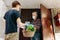 A grocery store delivery man wearing a black polo-shirt delivering food to an old man at home