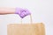 A grocery store delivery service worker gives a paper bag in a purple glove