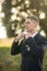 Groom adjusts the bow tie. Handsome man standing in the middle of field in the background of big tree