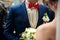 Groom in blue suit and red bow tie stands in the front of a bride