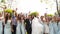 Groom, bride and excited friends cheering on camera on wedding day in park. Groomsmen and pretty bridesmaids in