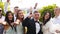 Groom, bride and excited friends cheering on camera on wedding day in park. Groomsmen and pretty bridesmaids in