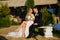 the groom and the bride in traditional wedding clothes sit on a park bench.