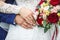 Groom embraces the bride with wedding red white rose bouquet. rings on the hands of newly-married couple