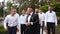 Groom flexing and having fun walking with groomsmen on wedding day. Happy classy man in black suit, bow tie and