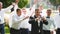 Groom flexing and having fun walking with groomsmen on wedding day. Happy classy man in black suit, bow tie and