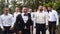 Groom flexing and having fun walking with groomsmen on wedding day. Happy classy man in black suit, bow tie and