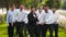 Groom flexing and having fun walking with groomsmen on wedding day. Happy classy man in black suit, bow tie and