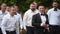 Groom flexing and having fun walking with groomsmen on wedding day. Happy classy man in black suit, bow tie and