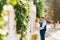 The groom gently hugs the bride against the backdrop of a beautiful white fence covered with ivy