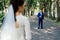 Groom is holding collar of his jacket outdoor with bride in blur in front of him