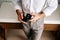 Groom is holding an open box with wedding rings in his hands, leaning against the table. Cropped. Faceless