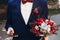 Groom holding phone and bouquet with red roses and succulents in