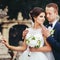 Groom holds shoulders of a stunning bride posing on the old back