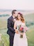 The groom is hugging the bride back while kissing on the forehead. Romantic portrait in the mountains.