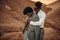 Groom hugs his bride dressed in his jacket in canyon at sunset a